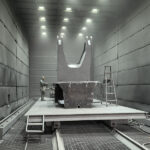 Manual sandblasting chamber operation on heavy steel H-beams using metallic grit abrasive media in a shipyard shot blasting booth.