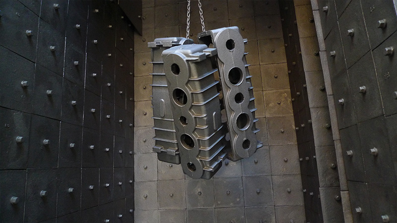 Heavy-scale valve body casting suspended by an automated industrial hook system, highlighting high-efficiency media penetration within complex internal cavities.