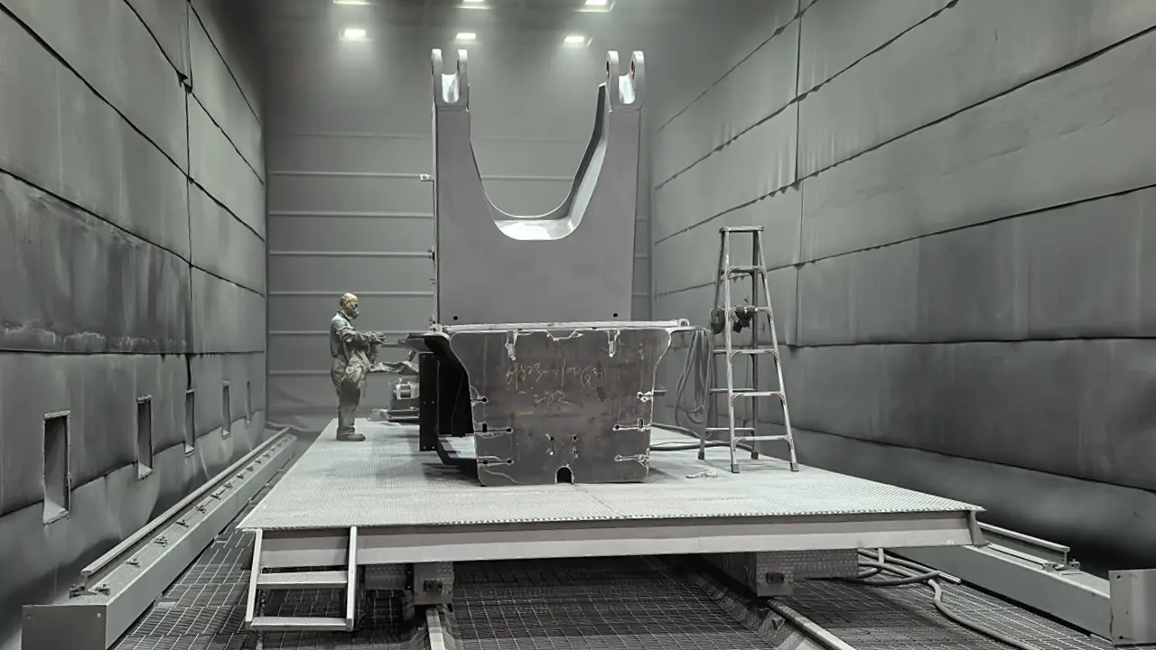 Manual abrasive blasting operation inside a custom sandblasting booth for heavy weldments